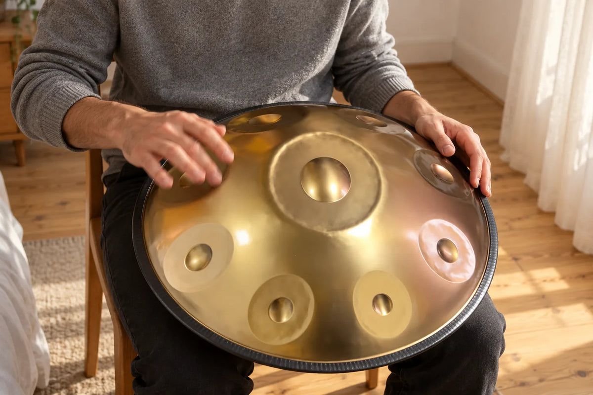 Des doigts rebondissent sur une note d'un handpan doré posé sur les genoux