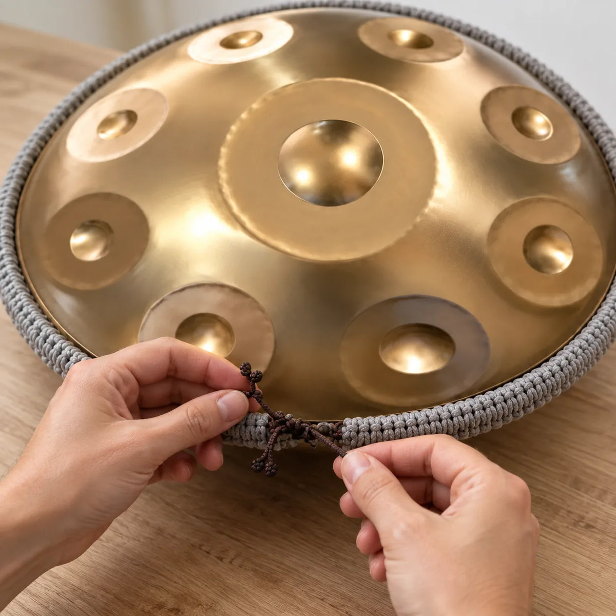 Deux mains nouent le cordon de protection tressé autour du bord d'un handpan doré