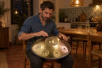Homme qui joue du handpan doré posé sur ses genoux, dans sa cuisine le soir