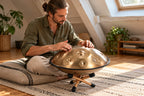 Homme assis en tailleur qui joue du handpan D Kurd doré posé sur le mini support en bois