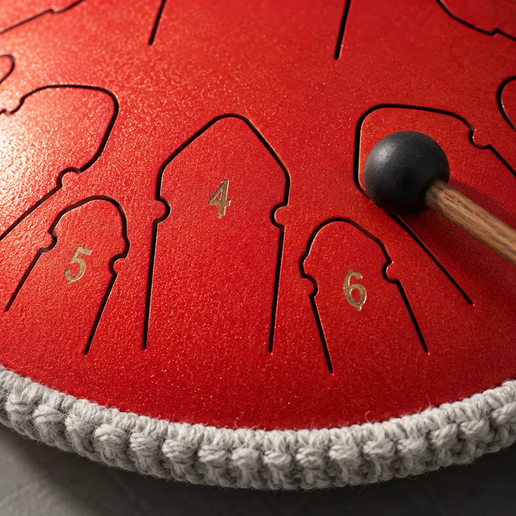 Gros plan sur les languettes chiffrées du tongue drum rouge et une mailloche
